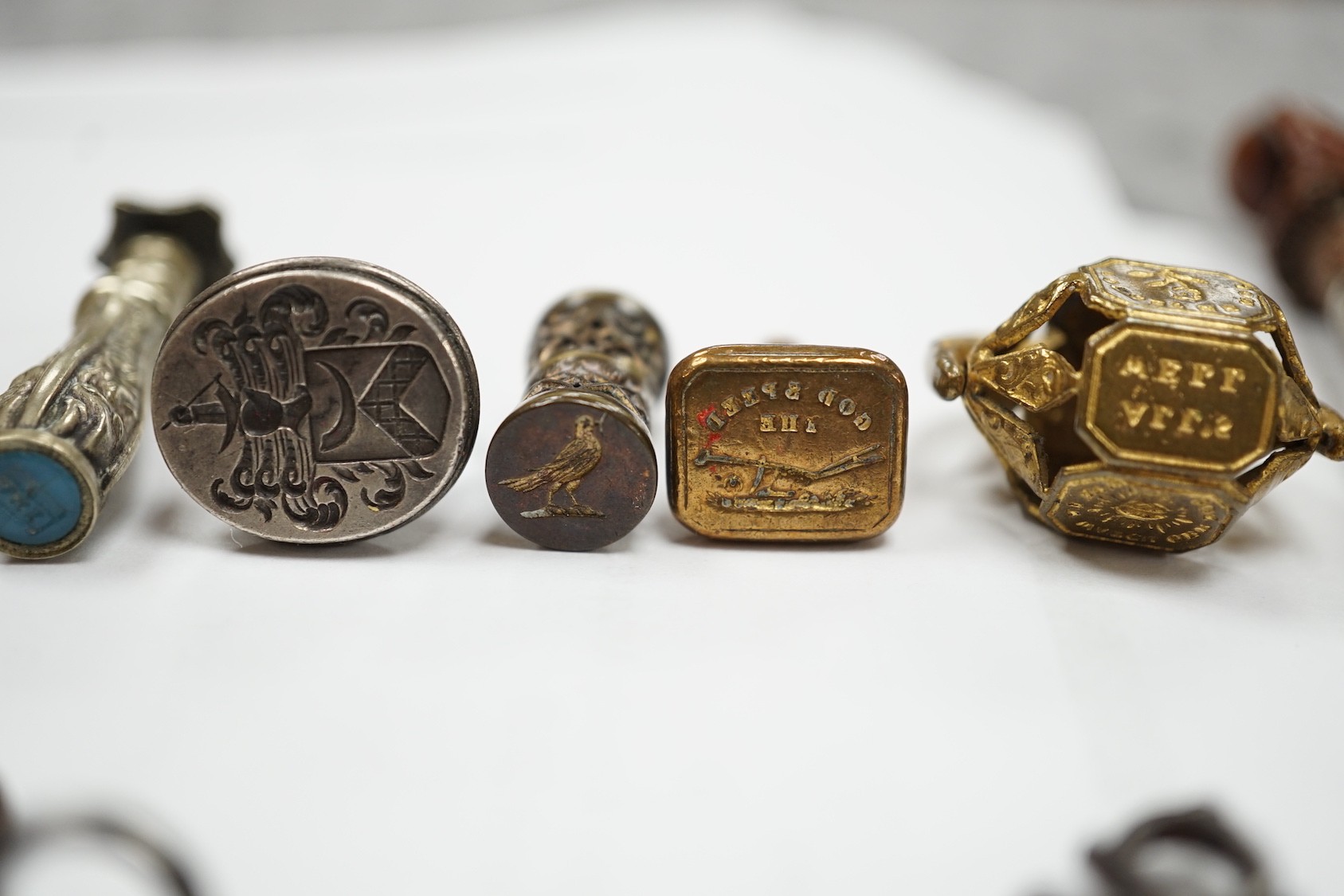 A group of twenty-five steel, gilt metal or nickel fob or desk seals, mostly 19th-century, including a steel swivel seal, a seal with boxwood finial modelled as a hand holding a ball and a nickel multi seal